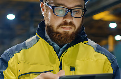 A person wearing a hard hat and glasses looking at a tablet